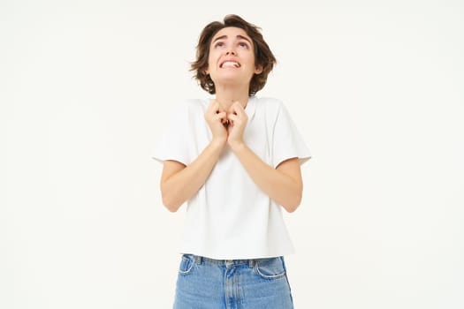 Portrait of girl looking with begging face, holding hands in pray, pleading, making wish, standing over white studio background.