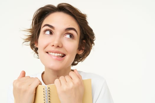 Portrait of happy woman with planner, holding notebook, reading notes and smiling, standing over white background.