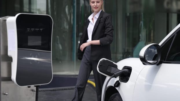 Progressive businesswoman unplug charger plug from charging station to his electric car before driving around city center. Eco friendly rechargeable car powered by sustainable and clean energy.