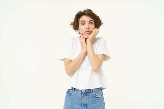 Portrait of woman standing over white background, looking shocked and concerned.