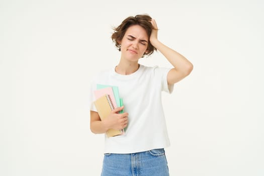 Troubled woman touches her head, looks upset, holds documents, standing frustrated against white studio background. Copy space