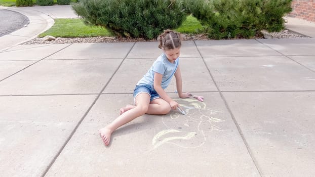 Little girl drawing chalk art on a suburban driveway on a summer day.