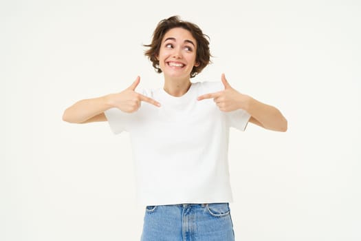 Image of confident, happy young woman, pointing at herself with smiling face, self-assured, standing over white background.