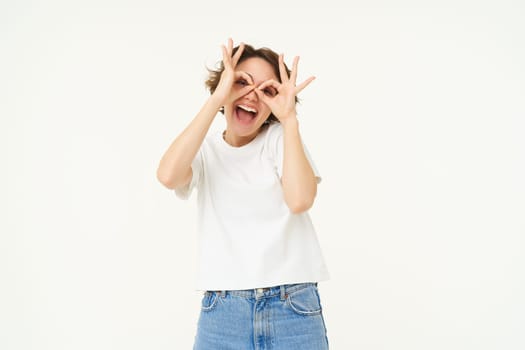 Portrait of carefree european woman, showing glasses with hands over eyes and smiling, posing over white background.