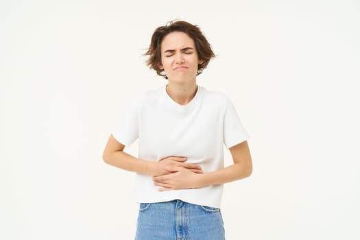 Image of woman with stomach ache, touching her belly, grimacing from pain or discomfort, has painful menstrual cramps, isolated over white background.