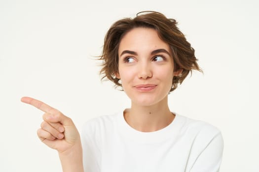 Image of candid brunette girl, pointing left, showing advertisement, recommending store, standing over white background. copy space