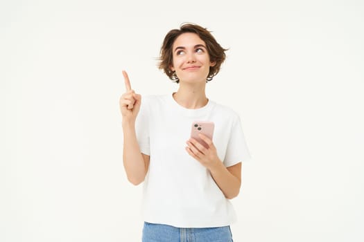 Portrait of woman with smartphone, using mobile phone and pointing at banner, showing text advertisement, standing isolated against white background.