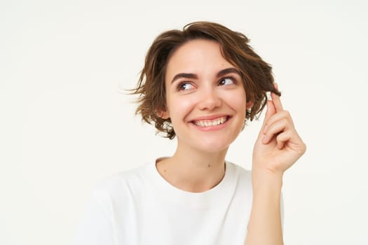 Close up of cute brunette girl playing with her hair, posing over white studio background.