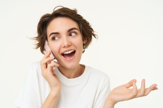 Portrait of happy, chatty young woman talking on mobile phone, using smartphone, calling someone, standing over white studio background.