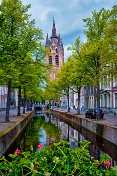 Delt canal with old houses bicycles and cars parked along and Oude Kerk Old church tower. Delft, Netherlands