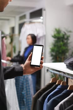 Clothing store customer man hand holding smartphone with blank white screen mockup, checking apparel on boutique website. Shopping mall client using mobile phone with empty touchscreen