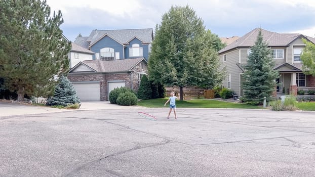 Little girl playing with a hula-hoop in a suburban cul-de-sac on a summer day.