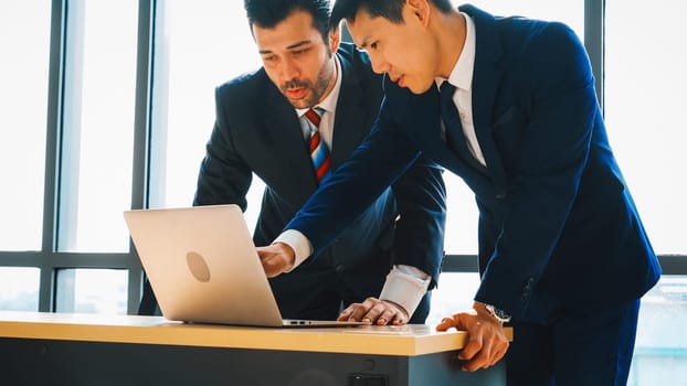 Two business people talk project strategy at office meeting room. Businessman discuss project planning with colleague at modern workplace while having conversation and advice on financial report. Jivy