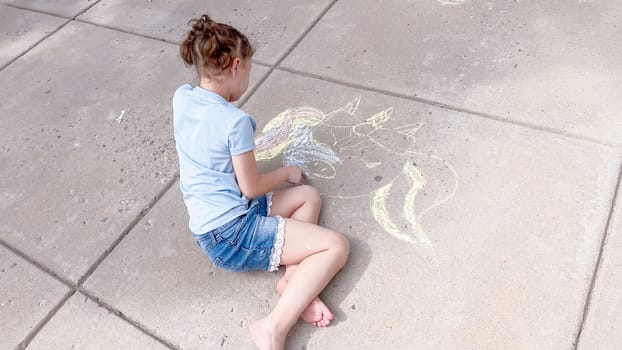 Little girl drawing chalk art on a suburban driveway on a summer day.