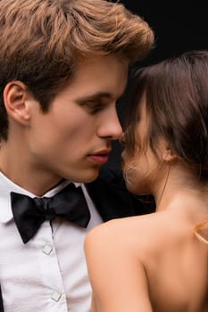 Handsome man in a suit and bowtie embracing his tattooed girlfirend topless in rearview shot