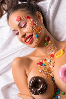 Brunette topless wearing red tanga with caramel makeup and bodyart and donuts on her breasts high angle shot