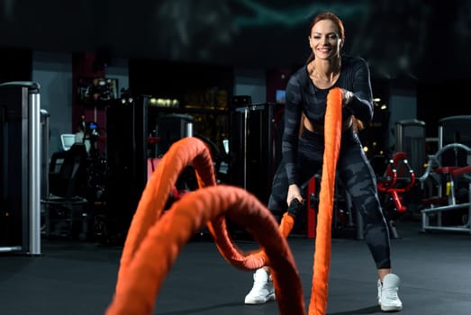 Slim brunette in sportswear doing exercises with a rope view in a gym