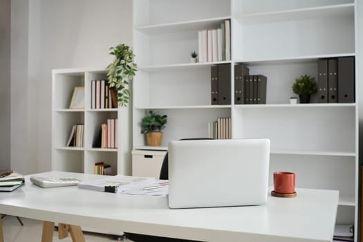 Laptop on white table with coffee cup, calculator and financial reports.