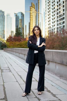 Professional hispanic businesswoman in black suit standing confidently in an urban environment with arms crossed.