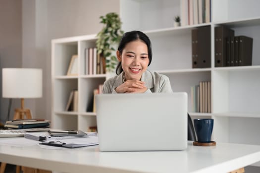 Charming businesswoman watching online webinar on laptop in office.