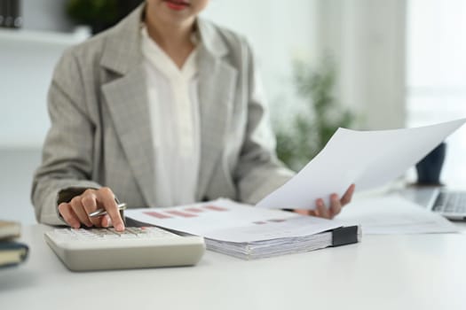 Businesswoman using a calculator and reviewing financial documents or reports.