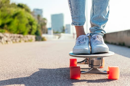 unrecognizable stylish skater in jeans and sneakers standing on skateboard on street on sunny day in summer