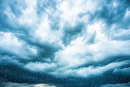 Raindrops are falling on glass with dark clouds and blue sky in the background