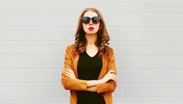 Fashion portrait pretty woman with crossed arms wearing a sunglasses, jacket over grey background