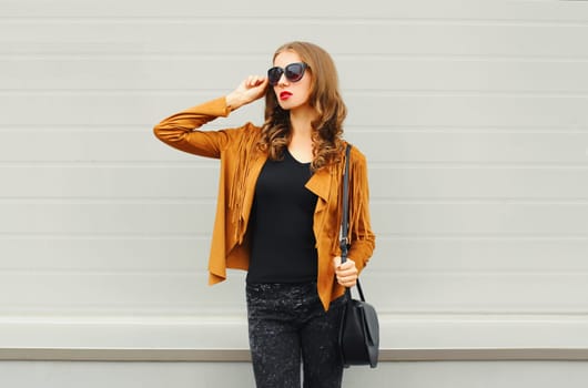Fashion young woman wearing a sunglasses jacket black handbag posing on grey background