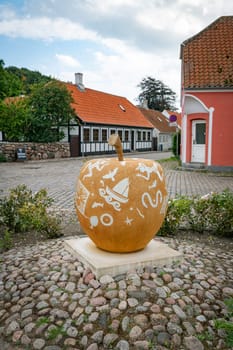 An artistic apple sculpture decorates the charming European town square of ebeltoft in denmark , surrounded by cobblestones and historic buildings, capturing a blend of creativity and tradition