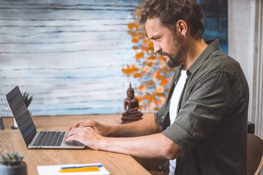 A man sitting at a table working on a laptop computer.