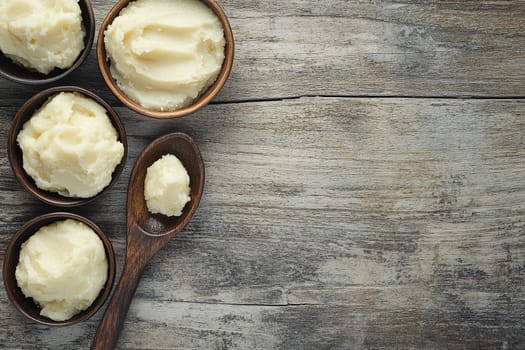 Rich, creamy butter is presented in wooden bowls on an aged wooden table, highlighting the artisanal process of butter making with a rustic charm.