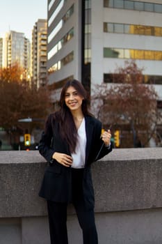 Hispanic businesswoman standing outdoors against an urban backdrop of office buildings and autumn trees.
