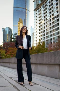 Portrait of hispanic businesswoman standing in an urban with tall glass buildings and autumn colored foliage.