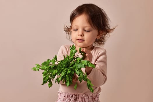 child girl holding fresh green parsley on beige background. healthy baby food.