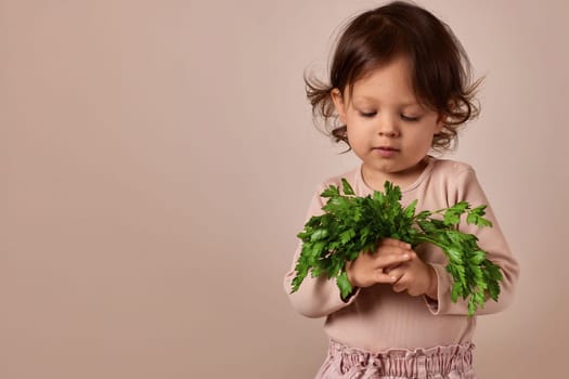 smiling child girl holding fresh green parsley on beige background. copy space