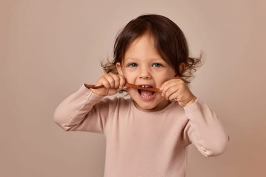 cute child girl bites fruit pastille on beige background. healthy baby food.