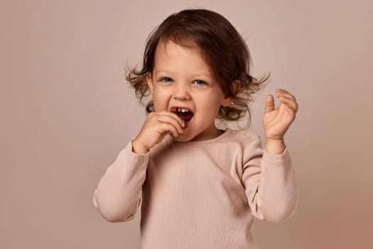 cute positive child girl eating fruit pastille on beige background. healthy baby food.