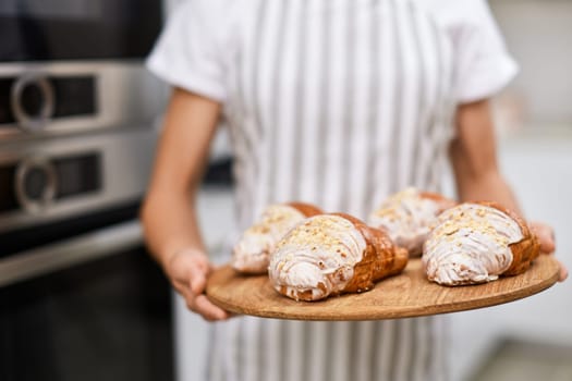 female baker holding wooden tray with freshly baked crispy golden croissants