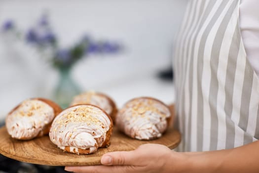 female baker holding wooden tray with freshly baked crispy golden croissants