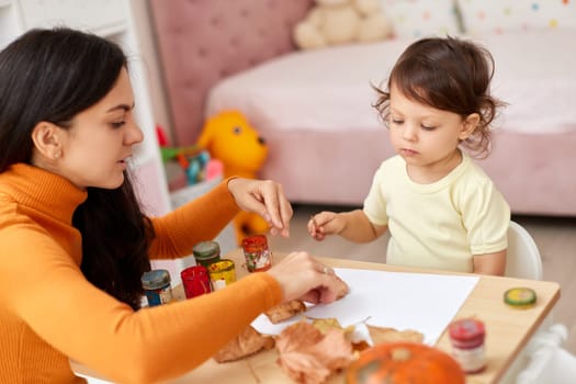happy little child girl and her mother drawing for the autumn holiday. Happy family making autumn decorations together