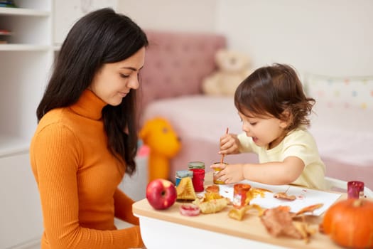 Cute little girl and mom spending good time painting autumn yellow leaves together