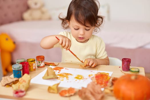 cute little child girl painting autumn leaves. baby girl drawing leaves in yellow and orange paint