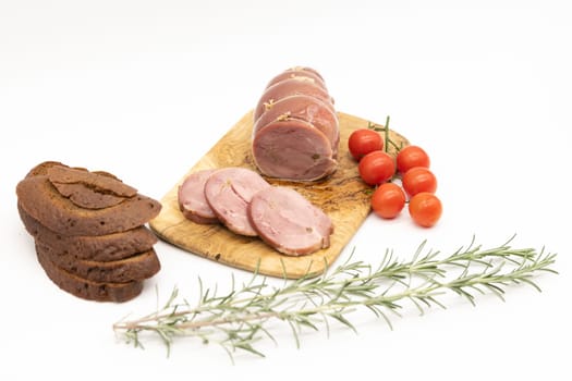 Baked Turkey roll with herbs, tomatoes and brown bread on a wooden background.