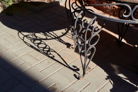A shadow on the sidewalk from a wrought-iron table on a sunny day.