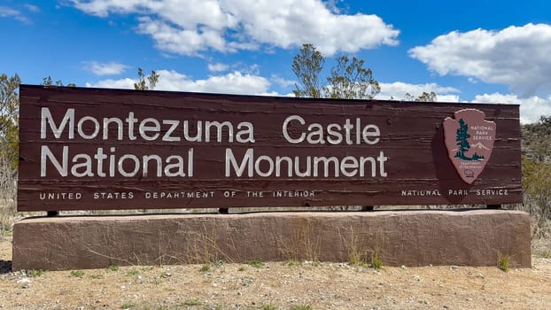 Camp Verde, Arizona, USA - 03.20.2024: Montezuma Castle National Monument entrance sign on a sunny day with blue skies and white clouds. The sign is made of wood.