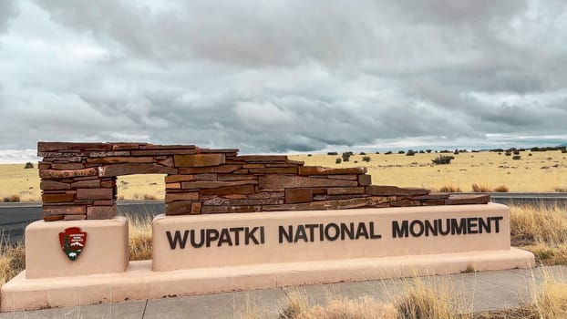 Flagstaff, Arizona, USA - 03.19.2024: Wupatki National Monument entrance sign on a cloudy day. The sign is surrounded by a desert landscape.