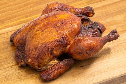 A beautifully roasted whole chicken, perfectly cooked, elegantly resting on a wooden cutting board surface