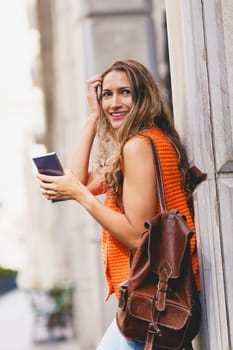 Vertical portrait of a latin woman carrying rucksack and holding a mobile in the city