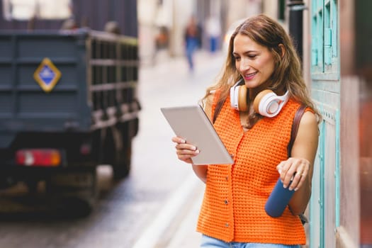 Latin woman holding reusable water bottle while using digital tablet standing in the city street